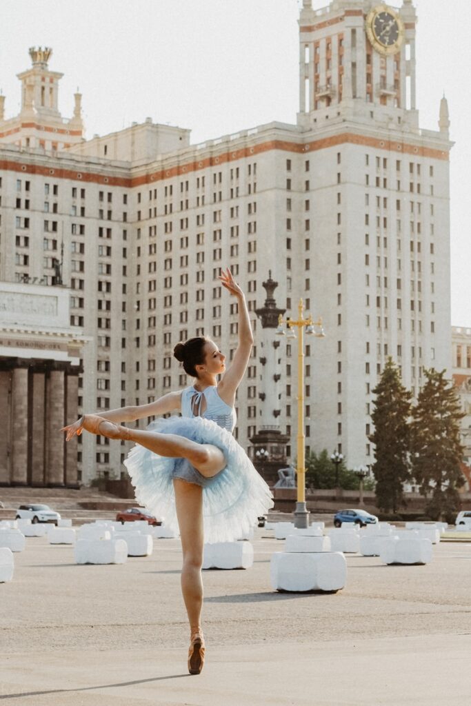 A ballerina performs an elegant dance near a white concrete building during daytime, symbolizing the evolution of dance traditions from medieval times to today.