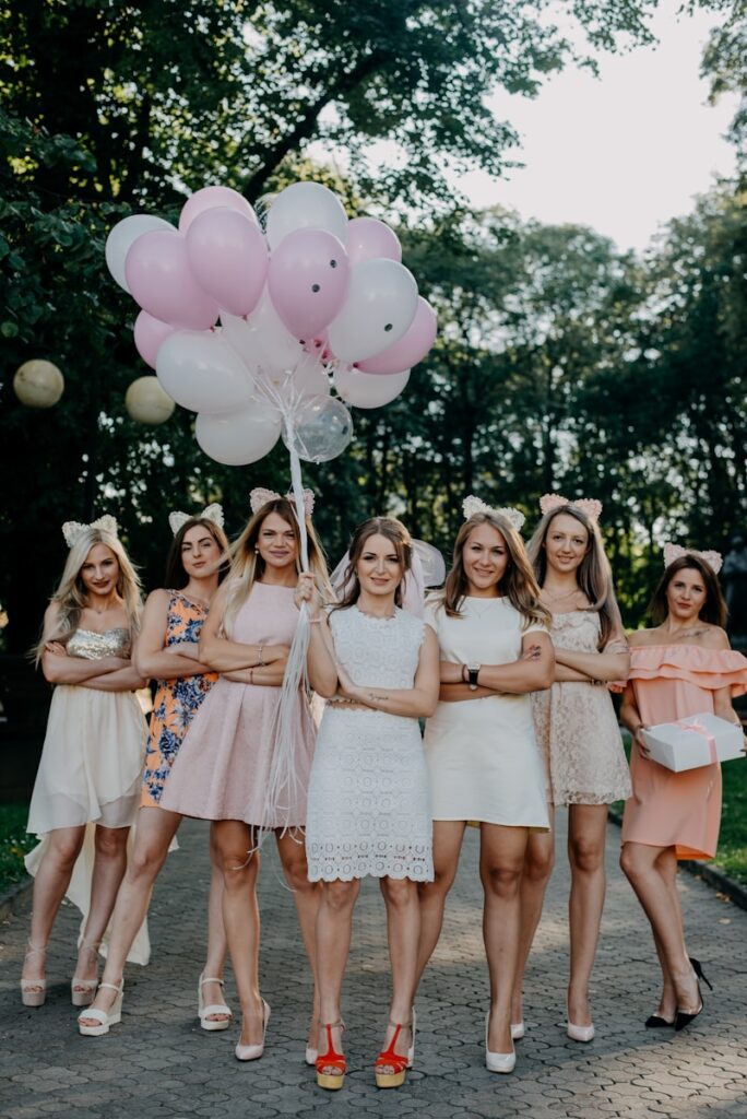 Bridesmaids standing side by side on a street during daytime, holding balloons, symbolizing the joy and excitement of involving the bridal squad in the wedding celebration.