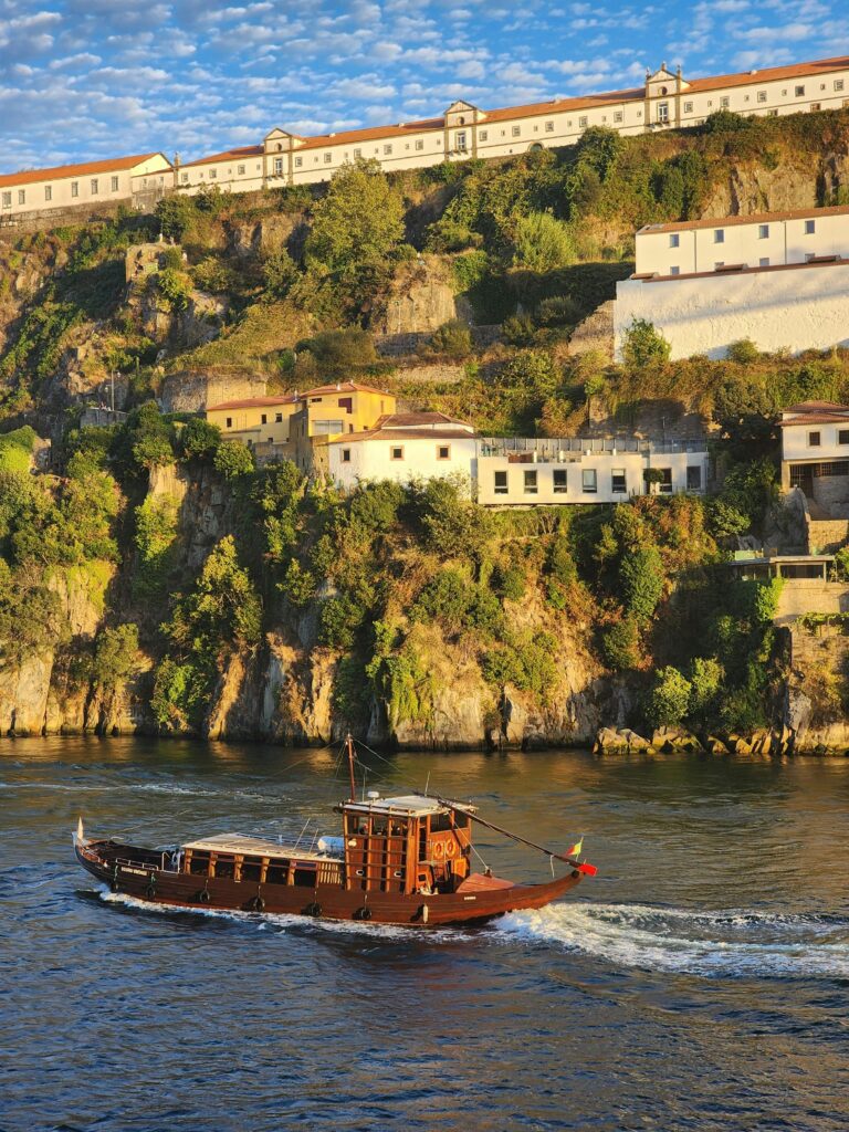 A traditional boat cruising on the scenic Douro River with hillside buildings in Porto, Portugal.